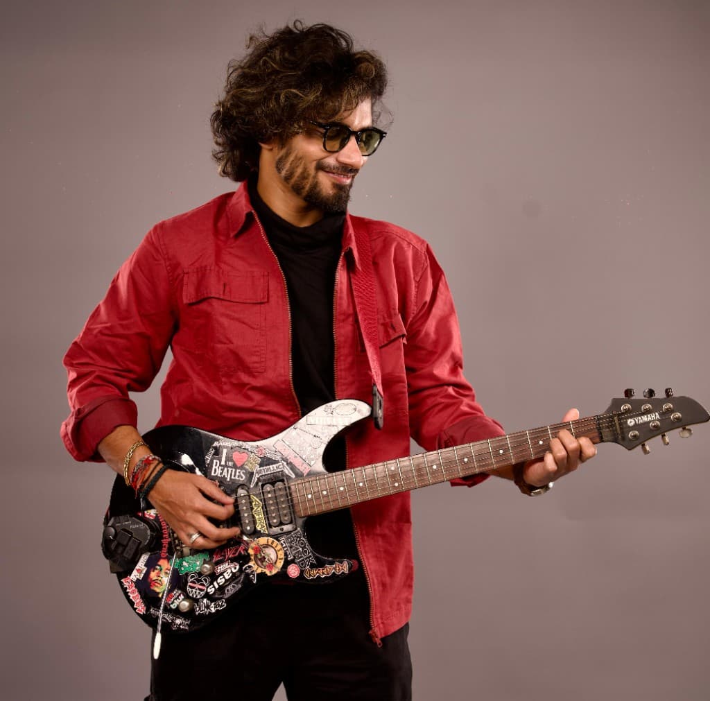 Sandy, a guitarist in a red shirt, holding a sticker-covered electric guitar